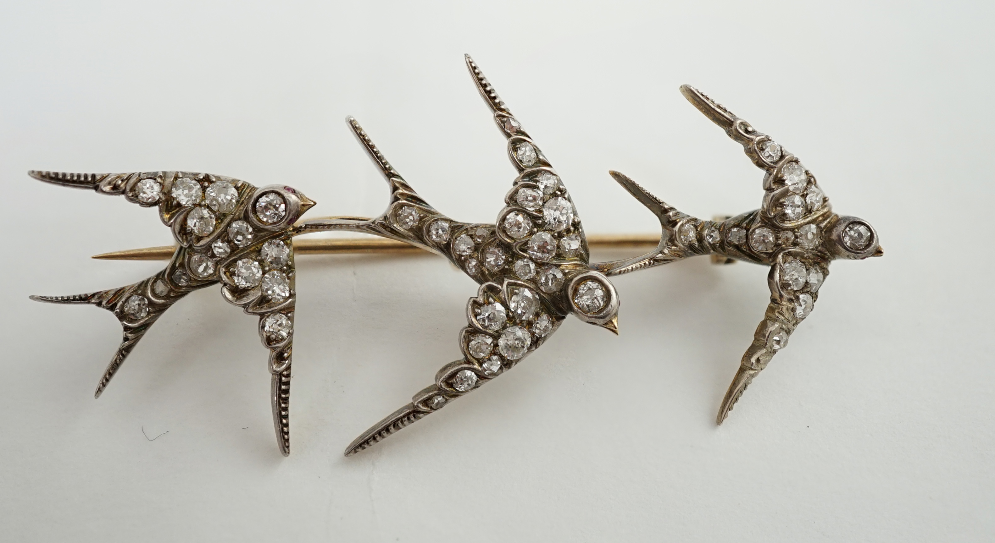 An Edwardian gold and graduated diamond cluster set triple swallow bar brooch